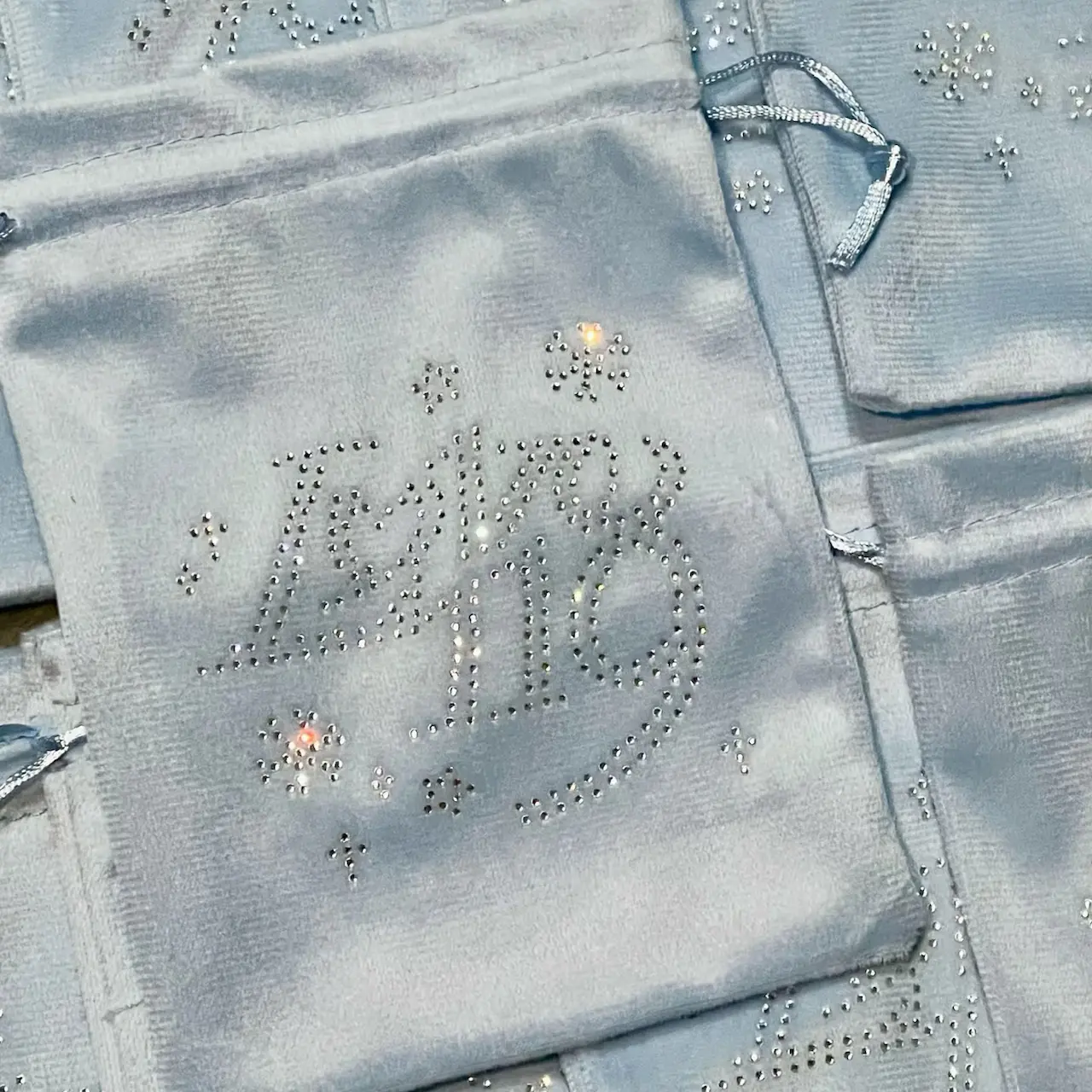 Light blue silk jewelry pouches with rhinestone logo decoration